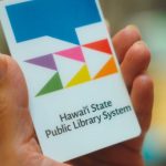 Hand holding a library card with the logo of the Hawaii State Public Library System