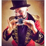 A person in a red jacket and top hat holding a glass ball.