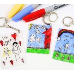 Three keychains featuring colorful children's art and assorted pens.