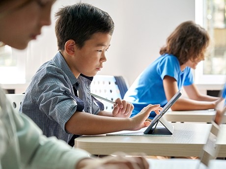 Male student seated in a classroom using an iPad tablet