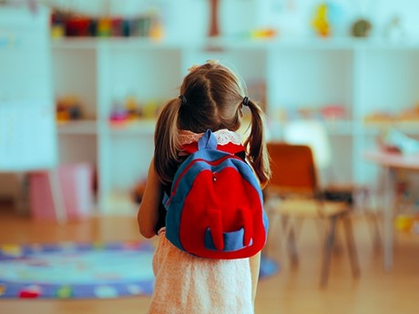Young girl with backpack arriving IN classroom
