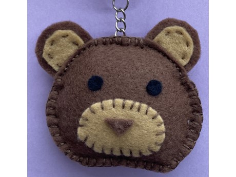 Handsewn, felt bear on a purple background. Only the head is shown. The head is dark brown and the nose and ears are light brown.