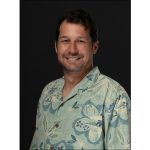 Headshot of man wearing aloha shirt with black background.
