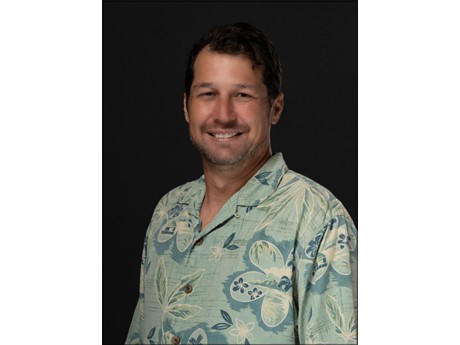 Headshot of man wearing aloha shirt with black background.