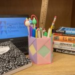 School supplies, books, and a laptop arranged on a desk. A colorful pencil holder is in the center.