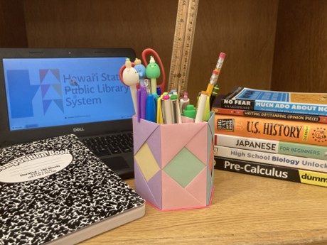 School supplies, books, and a laptop arranged on a desk. A colorful pencil holder is in the center.