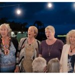 4 women singing outside at night, light bulbs above