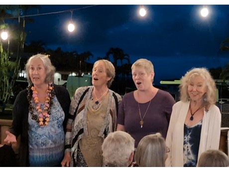4 women singing outside at night, light bulbs above