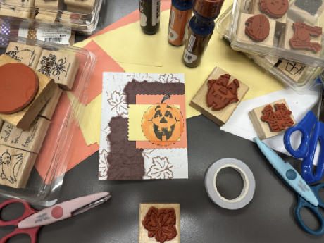 card with jack-o-lantern stamped image surrounded by stamps, paper, tape, scissors, and ink