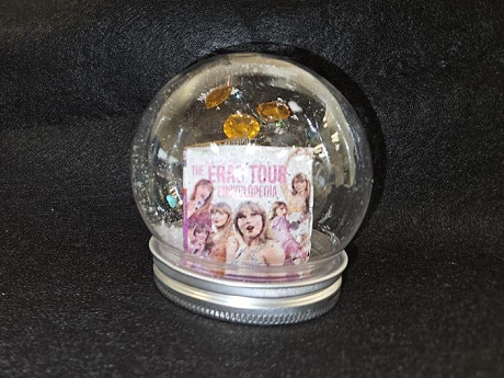 a waterless slon gllobe with a mini mock taylor swift book and gems inside, black background