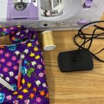 sewing machine with cord, seam ripper, yellow spool of thread and a purple patterned bag