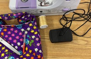 sewing machine with cord, seam ripper, yellow spool of thread and a purple patterned bag