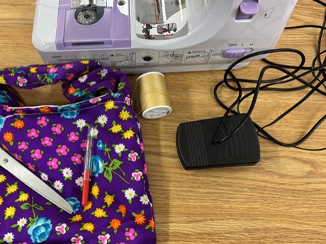 sewing machine with cord, seam ripper, yellow spool of thread and a purple patterned bag