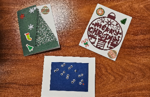 three handmade Christmas cards, a tree, an ornament, and reindeer eyes