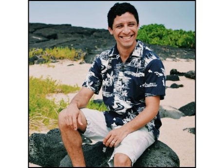 Man sitting on beach rocks, aloha shirt, white shorts, black hair