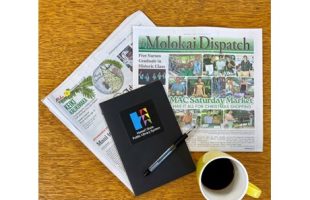 A wooden table holds two folded newspapers, a black notebook with a pen featuring a colorful logo, and a yellow mug filled with coffee.