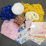 Assorted scrap materials for crafting including yarn, fabric scraps, card stock, washi tape