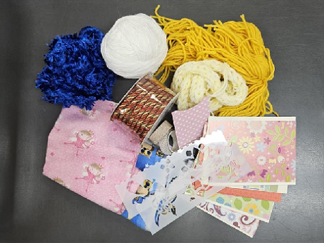 Assorted scrap materials for crafting including yarn, fabric scraps, card stock, washi tape