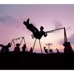 Multiple kids are swinging on swing sets at dusk.
