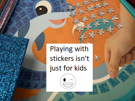 picture of dolphin with shiny stickers and stars being added by hand and text playing with stickers isn't just for kids and winking smiley face