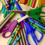 a pile of school supplies including scissors, crayons, and marker pens