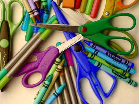 a pile of school supplies including scissors, crayons, and marker pens