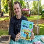 Benjamin Fairfield sitting at a park table holding a copy of his book Kani Ka Opala (How can garbage sing?).