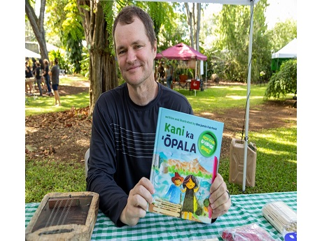 Benjamin Fairfield sitting at a park table holding a copy of his book Kani Ka Opala (How can garbage sing?).