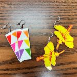 Two pairs of earrings featuring the HSPLS logos, one with colorful triangles and one with the yellow hibiscus.