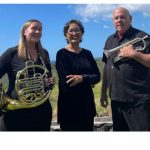 3 musicians, 2 female, 1 male, wearing black, holding a french horn and a trumpet