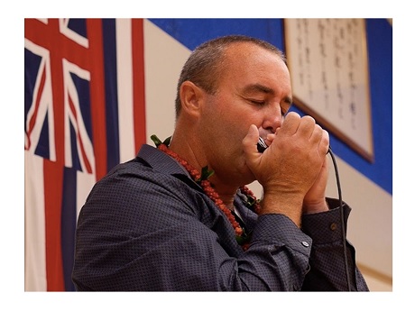 Color photo of Danilo Marrone playing a harmonica in front of a backdrop of international flags