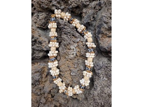 A lei made of shells, nuts, and small woven boxes lays adorns a rock wall