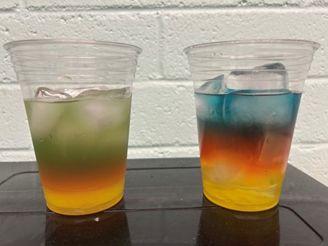 2 clear cups of layered rainbow limeade. The bottom layer of both cups is yellow and the middle layer of both cups is orange. The top layer for the cup on the left is green and the top layer for the cup on the right is blue.