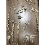 Various intricate palm leaf creations are arranged on a wooden table. The crafts include woven fish and roses.