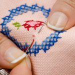 hands holding needle with thread stitching into cloth