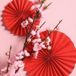 Two red fans and a pink cherry blossom branch set against a pink background