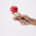 picture of a hand holding a red and tan wooden kendama toy