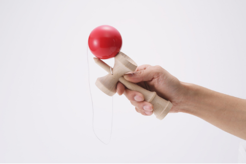 picture of a hand holding a red and tan wooden kendama toy