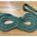 Green crocheted masquerade mask laid flat on brown table.
