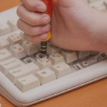 hand holding a tool to extract keys from a computer keyboard