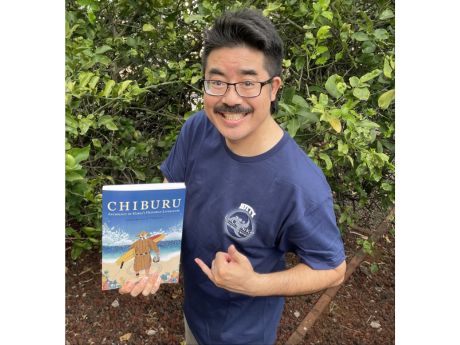 Poet Laureate Lee A. Tonouchi holding the book Chiburu and giving a shaka