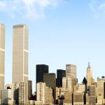 Historic New York City skyline featuring the twin World Trade Center towers, dense Manhattan skyscrapers, and a bright blue sky.