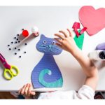 photo of a cat made of colored paper and googly eyes with a child's hand hovering above