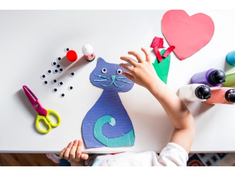 photo of a cat made of colored paper and googly eyes with a child's hand hovering above